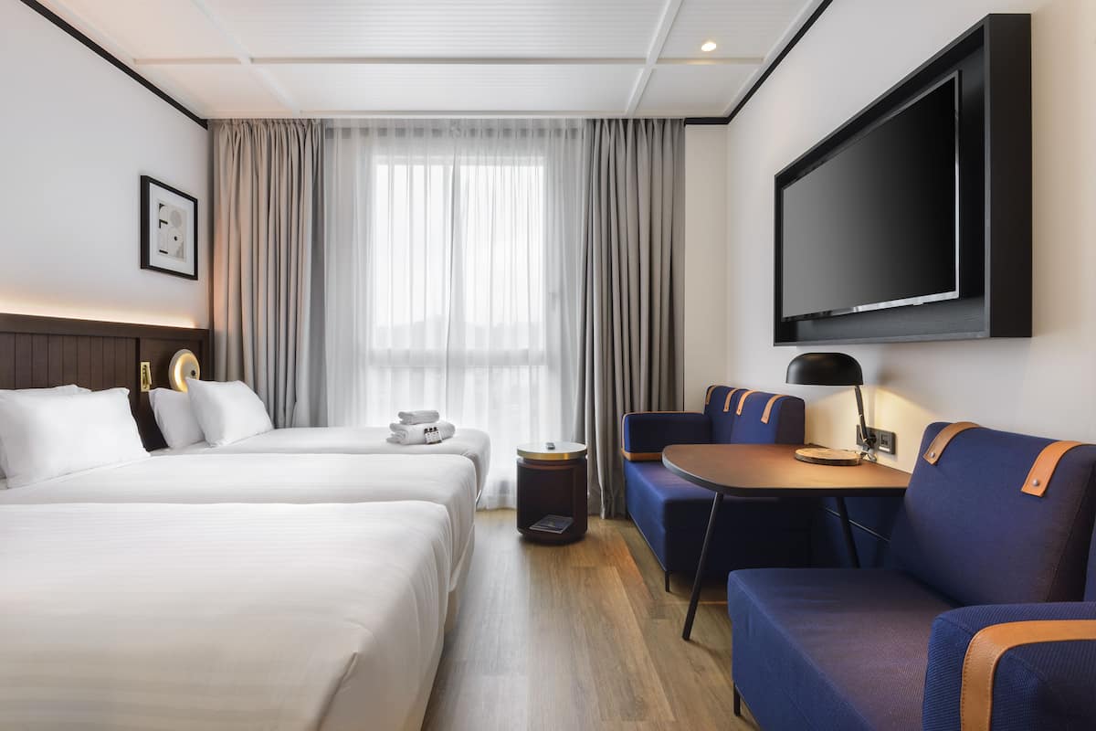 Une chambre d’hôtel avec deux lits, une télévision, un bureau avec une lampe et un canapé.