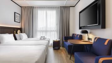 Una habitación de hotel con dos camas, televisión, escritorio con lámpara y sofá.