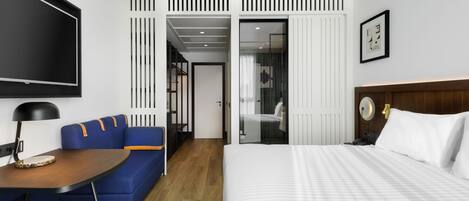 Habitación de hotel con cama, sofá, televisor, escritorio y puerta que da a un baño.