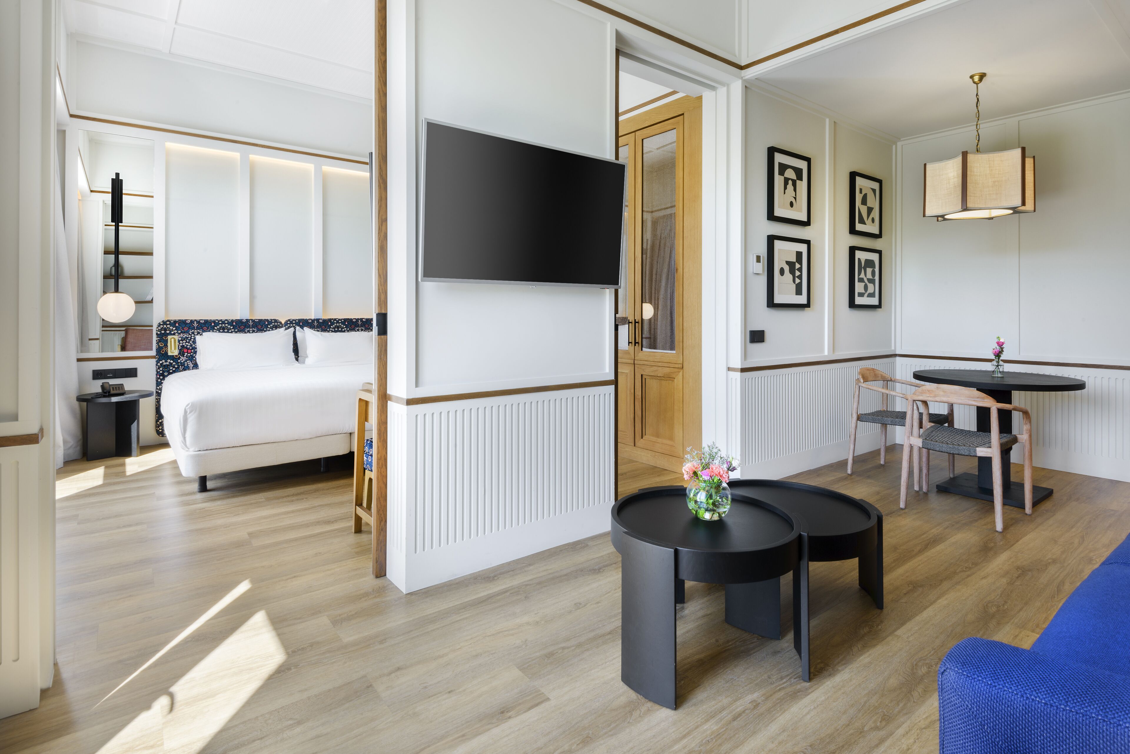 Een moderne hotelkamer met een bed, een flatscreen televisie, een zithoek met een tafel en stoelen, en een blauwe bank.