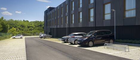 A parking area with several cars parked in front of a modern building with large windows and a flat roof.