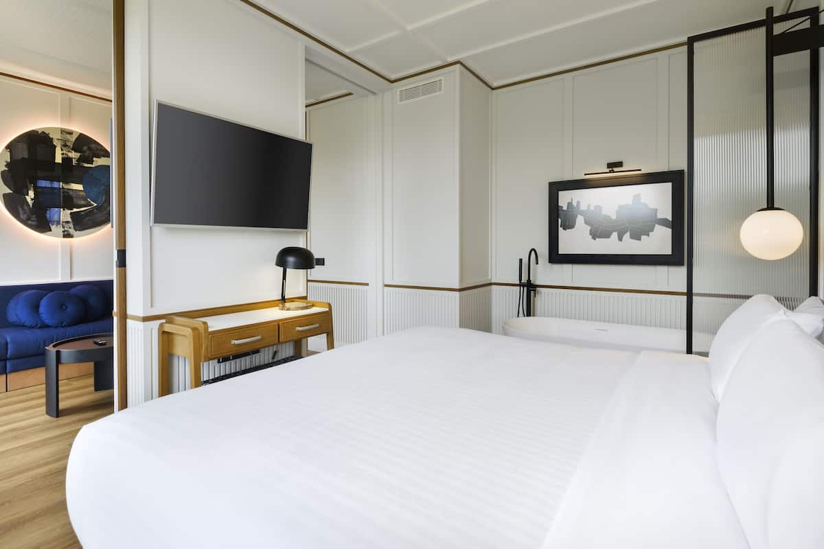 Une chambre d’hôtel avec un grand lit, un bureau en bois, un canapé bleu, un téléviseur à écran plat et un tableau encadré au mur.