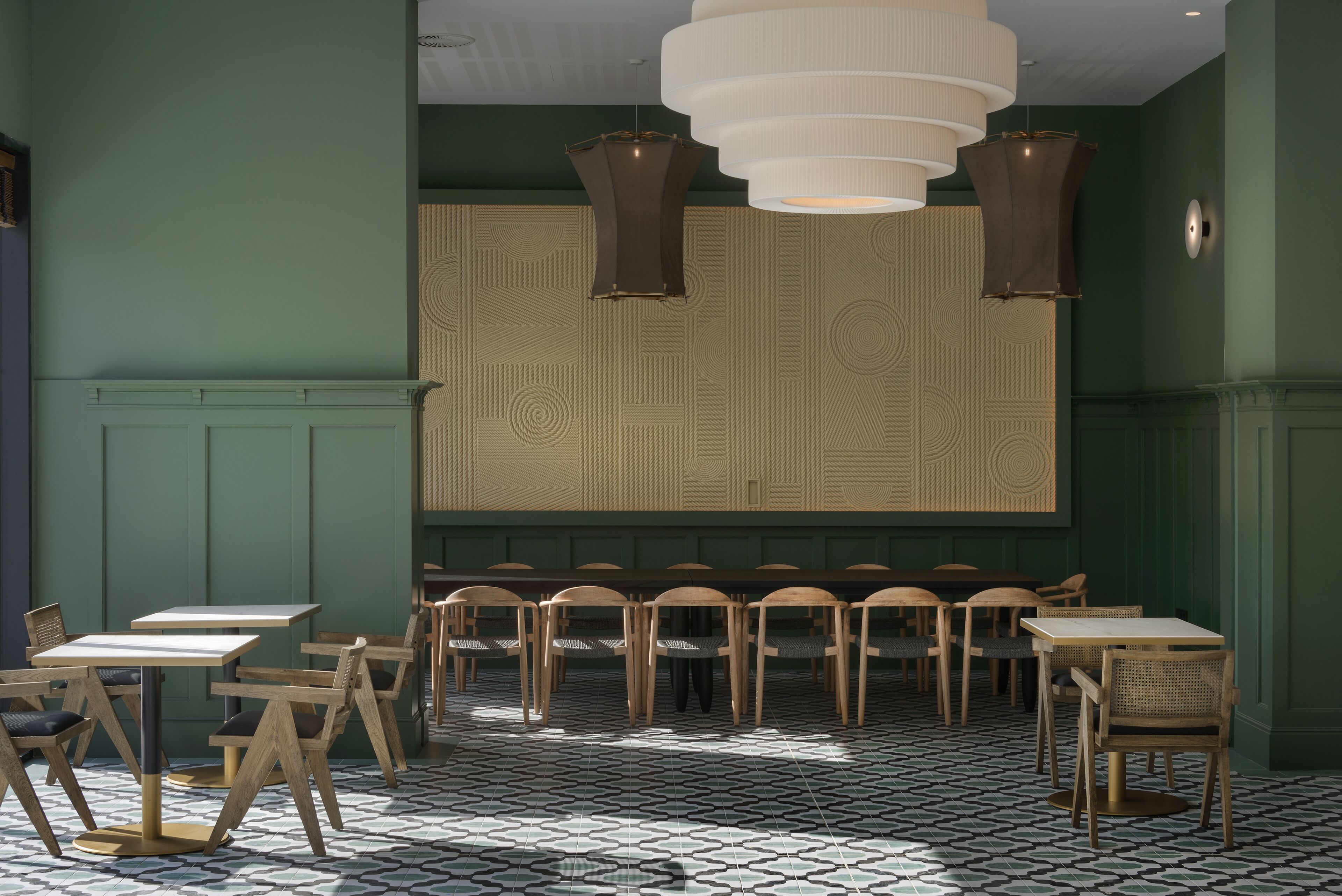 A dining area with tables and chairs, patterned wallpaper, and pendant lighting.