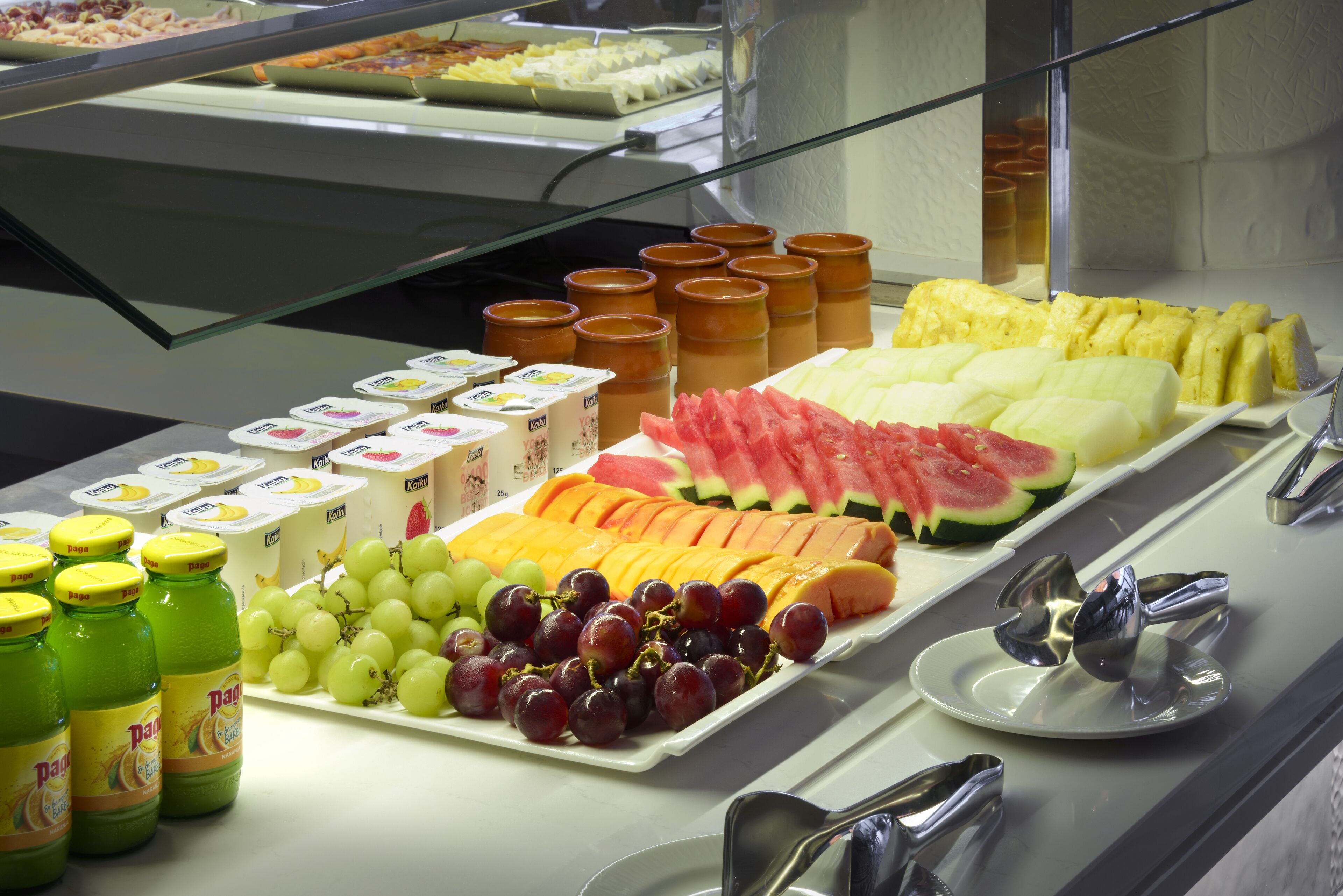 Un bufé con diversas frutas, yogur y zumo.