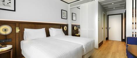 A hotel room with a large bed, bedside tables with lamps, a wooden headboard, and a door leading to another room.