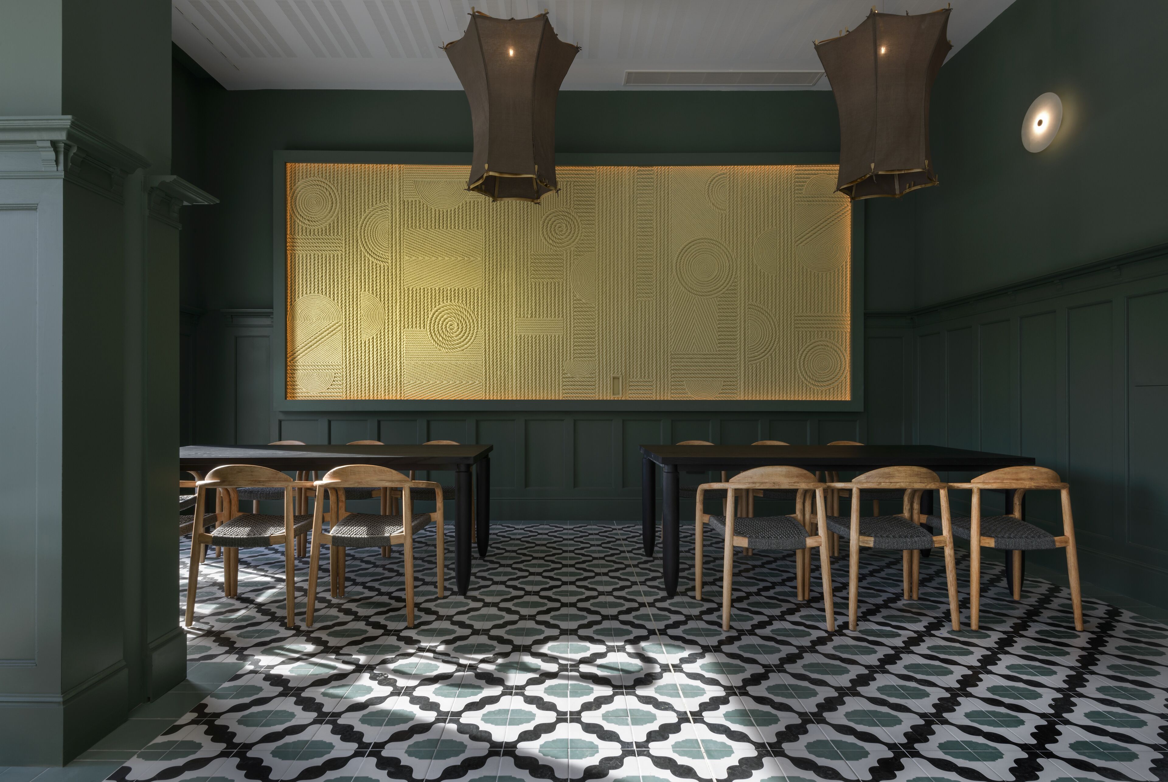 Una habitación con piso estampado, sillas de madera, una mesa y un panel decorativo en la pared.