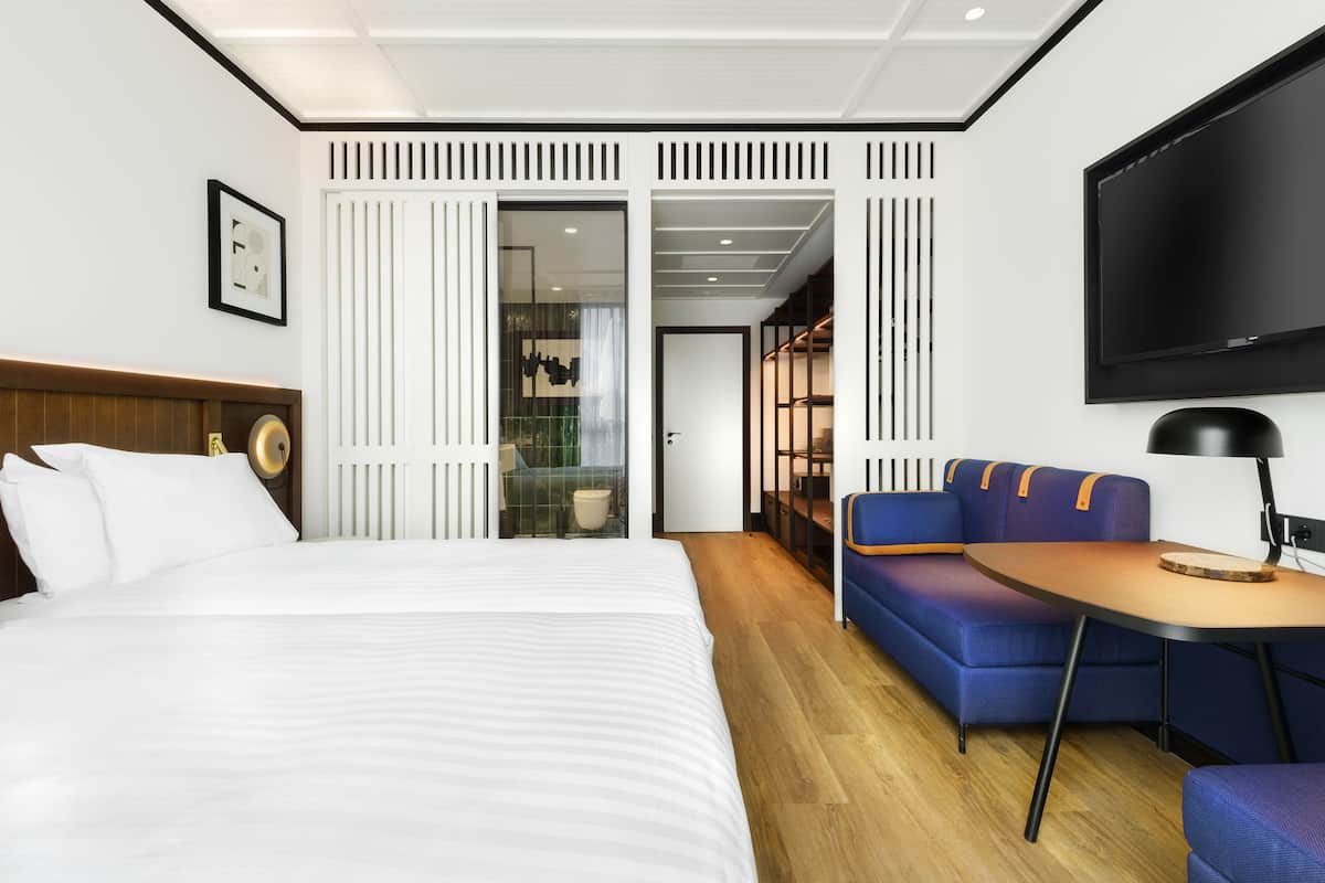 Une chambre d’hôtel moderne avec un grand lit, un canapé, une petite table et un téléviseur.