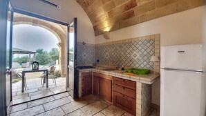 A kitchen with a stone archway leading to an outdoor patio, a tiled backsplash, wooden cabinets, and a white refrigerator. - 3-apt house with private pool, 250m from beach (Torre Vado)