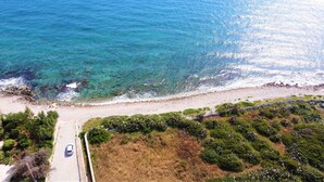 An aerial view of a coastal road with a car, clear blue sea, rocky beach, and dense greenery. - 3-apt house with private pool, 250m from beach (Torre Vado)