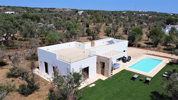 Una casa moderna de dos pisos con piscina, rodeada de césped cuidado y vegetación escasa.