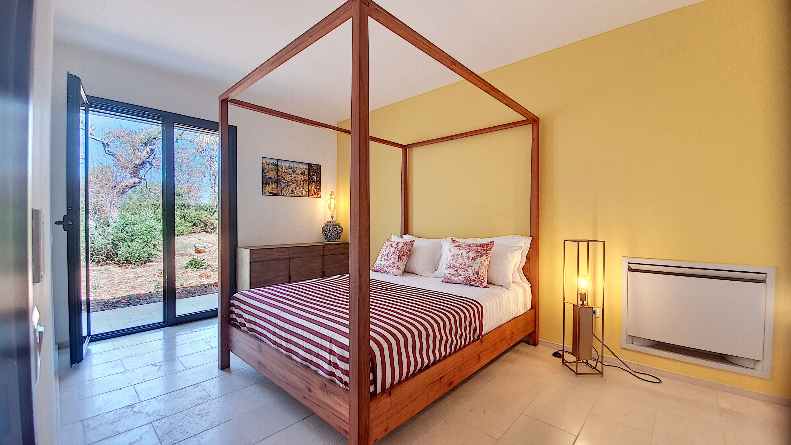 Une chambre à coucher avec un lit à baldaquin, une table de chevet avec une lampe et une vue sur l’extérieur grâce à une porte-fenêtre coulissante.