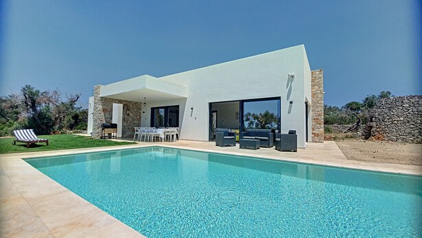 A modern house with a swimming pool, outdoor furniture, and a stone wall.
