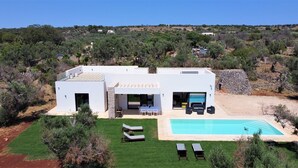 A modern two-story house with a swimming pool, outdoor seating, and a view of the surrounding landscape.