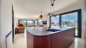 A modern kitchen with a large island, large windows, and a view of the outdoors.