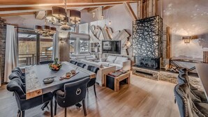A cozy, rustic living room with a wooden ceiling, a fireplace, and a large TV.
