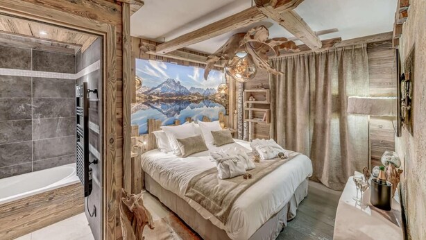 A bedroom with a large bed, a wooden ceiling, a mural of mountains, and a bathtub.