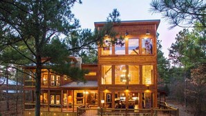 A multi-story wooden cabin with large windows and a deck area.