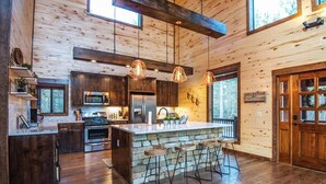 A modern kitchen with wooden walls, a large island with bar stools, and pendant lighting.