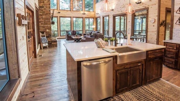 A spacious kitchen with a large island, wooden walls, and large windows offering views of the outdoors.