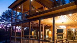 A two-story wooden cabin with a balcony, a fireplace, and a television.