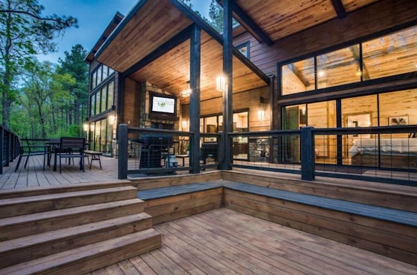 A modern log cabin with a deck, large windows, and a TV screen.