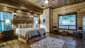 A wooden cabin bedroom with a bed, two nightstands, a ceiling fan, and large windows. - "Rustic Mountain Lodge" Bunk Room, Outdoor Entertaining, Pets (Broken Bow)