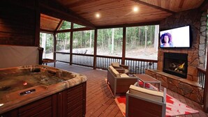 Una terraza de madera con jacuzzi, mobiliario exterior y chimenea de piedra.