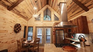 Interior acogedor de una cabaña con comedor, cocina y una gran chimenea.