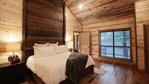Un dormitorio tipo cabaña de madera con una cama grande, una mesita de noche, una ventana con vistas y techo de madera.