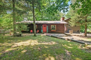 A rustic cabin with a red door, surrounded by trees and a well-maintained lawn. - Sunset Cabin - Secluded retreat on Beaver Lake (Rogers)