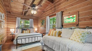A cabin-style bedroom with a bed, a sofa, a ceiling fan, and a stained glass window.