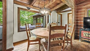 A rustic wooden dining area with a round table and chairs, a chandelier, and a television on a side table.