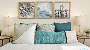 Un lit avec une literie à rayures, plusieurs oreillers et des tableaux encadrés accrochés au mur.