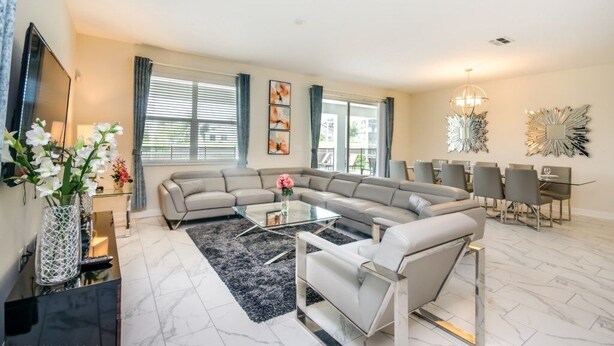 Un salon moderne avec un canapé d’angle, une table basse en verre et un coin repas agrémenté d’un lustre.