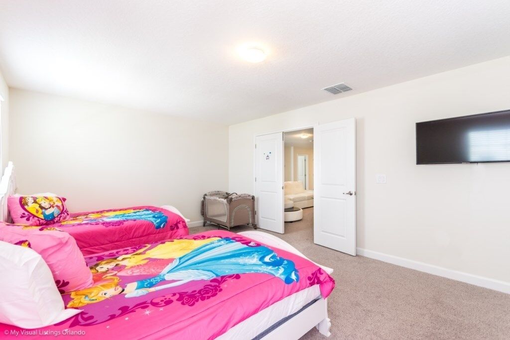 A bedroom with two beds, a TV on the wall, and a door leading to another room.