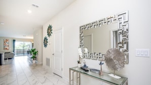 Un couloir moderne avec une console en verre, des miroirs décoratifs et une porte donnant sur une autre pièce.