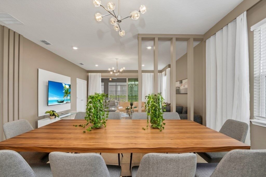 A modern conference room with a wooden table, grey chairs, a chandelier, and potted plants.