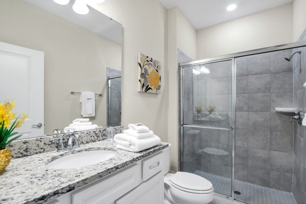 Une salle de bain moderne avec un lavabo surmonté d’un plan de travail en granit, des toilettes blanches et une douche à parois de verre.