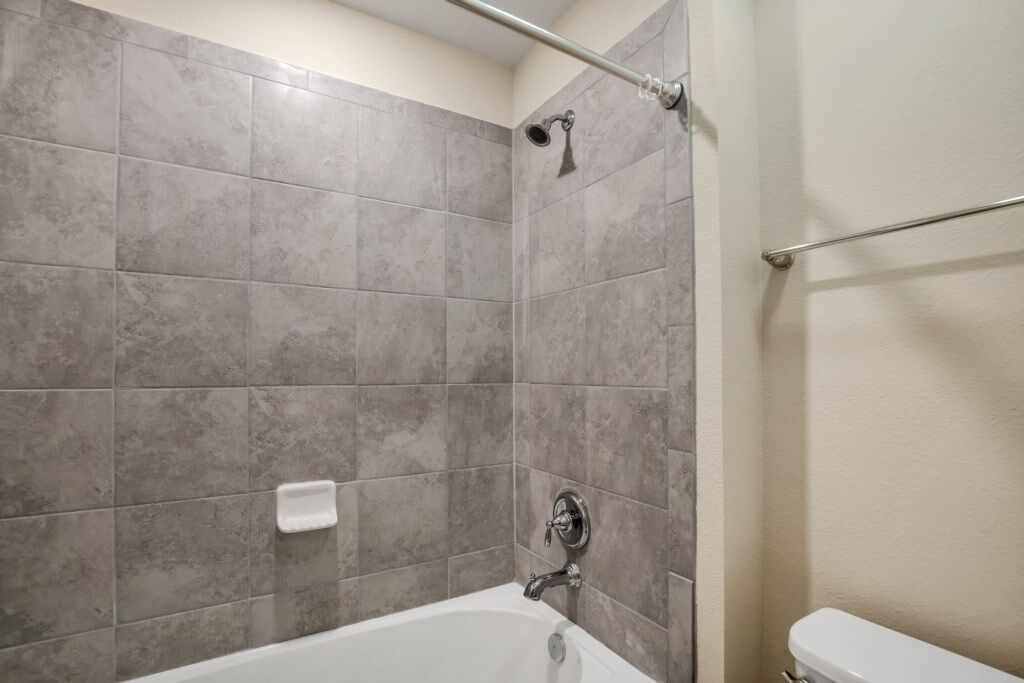 A bathroom with a bathtub, a showerhead, and a toilet.