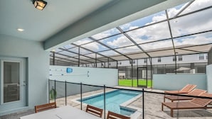 Un espace extérieur abrité comprenant une piscine, des chaises longues et une table.