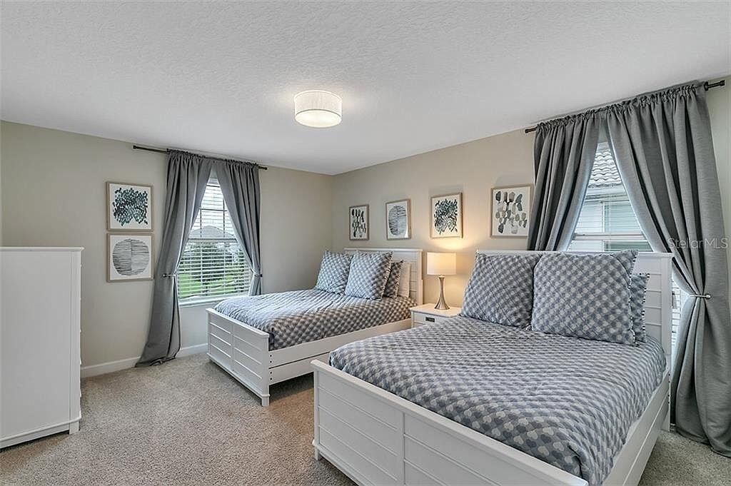 A bedroom with two beds, a nightstand, a lamp, and a dresser.