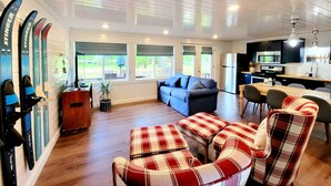 A spacious living area with a sofa and plaid chairs, a kitchen with modern appliances, and large windows offering views of the outdoors.