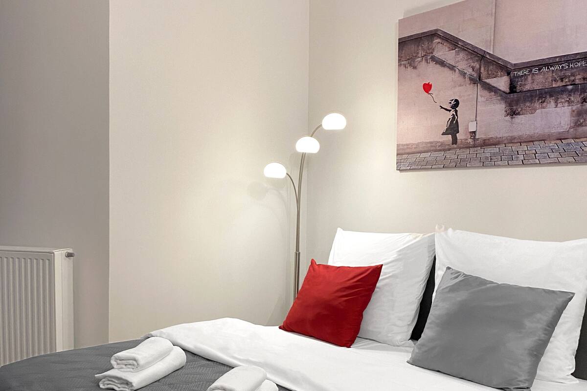 A neatly made bed with white and gray linens, a red pillow, and two folded towels on the bed.