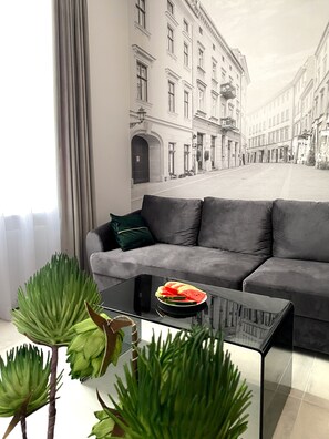 A modern living room with a grey sofa, a glass coffee table with a watermelon slice, and green plants. - Starowiślna 41-43 by PI Apartments (Kraków)