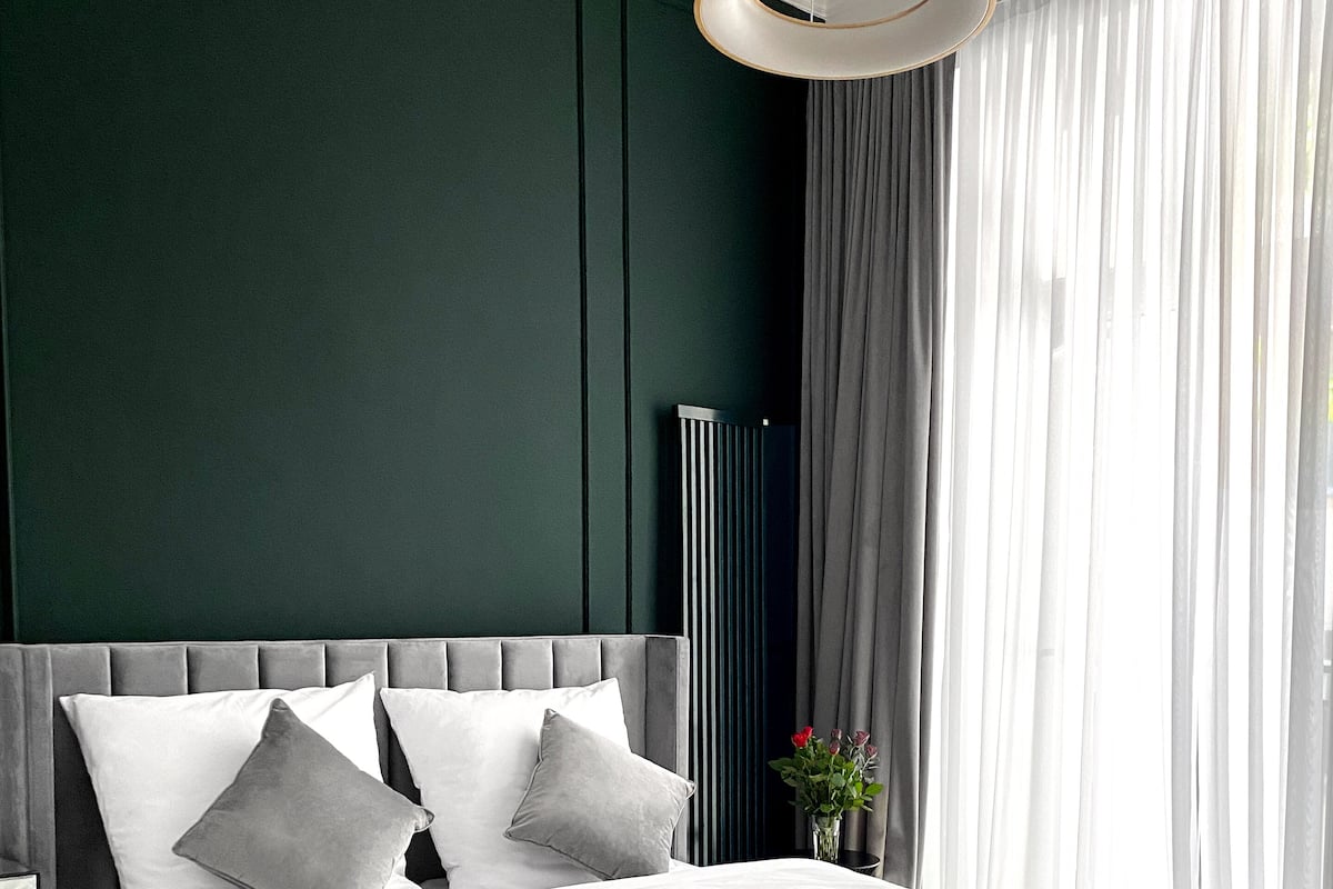 A modern bedroom with a grey bed, white bedding, and a grey accent wall.
