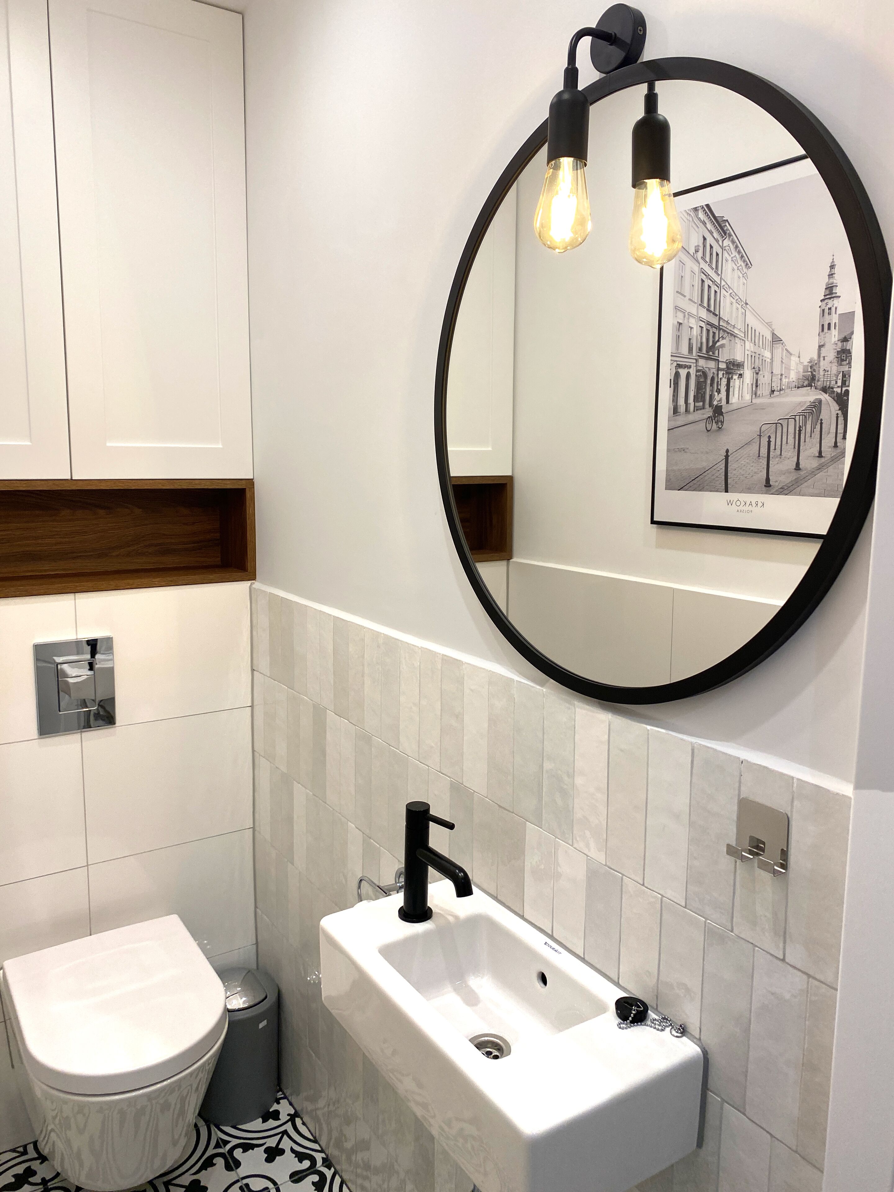Ein modernes Badezimmer mit einer weißen Toilette, einem rechteckigen Waschbecken und einem Spiegel mit schwarzem Rahmen.