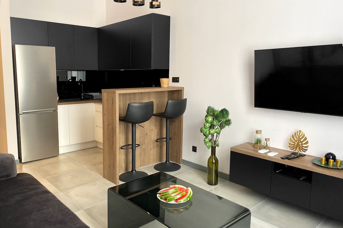 A modern kitchen with black cabinets, a stainless steel refrigerator, and a wooden island with two black bar stools.