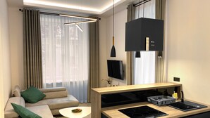 A modern living room with a sofa, a coffee table, a TV, and a kitchen area with a stove and cabinets. - Starowiślna 41-43 by PI Apartments (Kraków)
