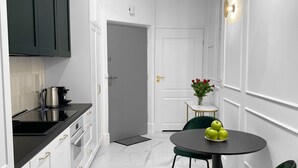 A modern kitchen with white cabinets, a black countertop, and a marble floor. There is a dining area with a round table and green chairs. - Starowiślna 41-43 by PI Apartments (Kraków)