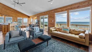 A spacious living area with a large window overlooking the ocean, a ceiling fan, and a wooden interior. - Oceanfront Dog Friendly Home w/ Hot Tub & Grill (Avon)